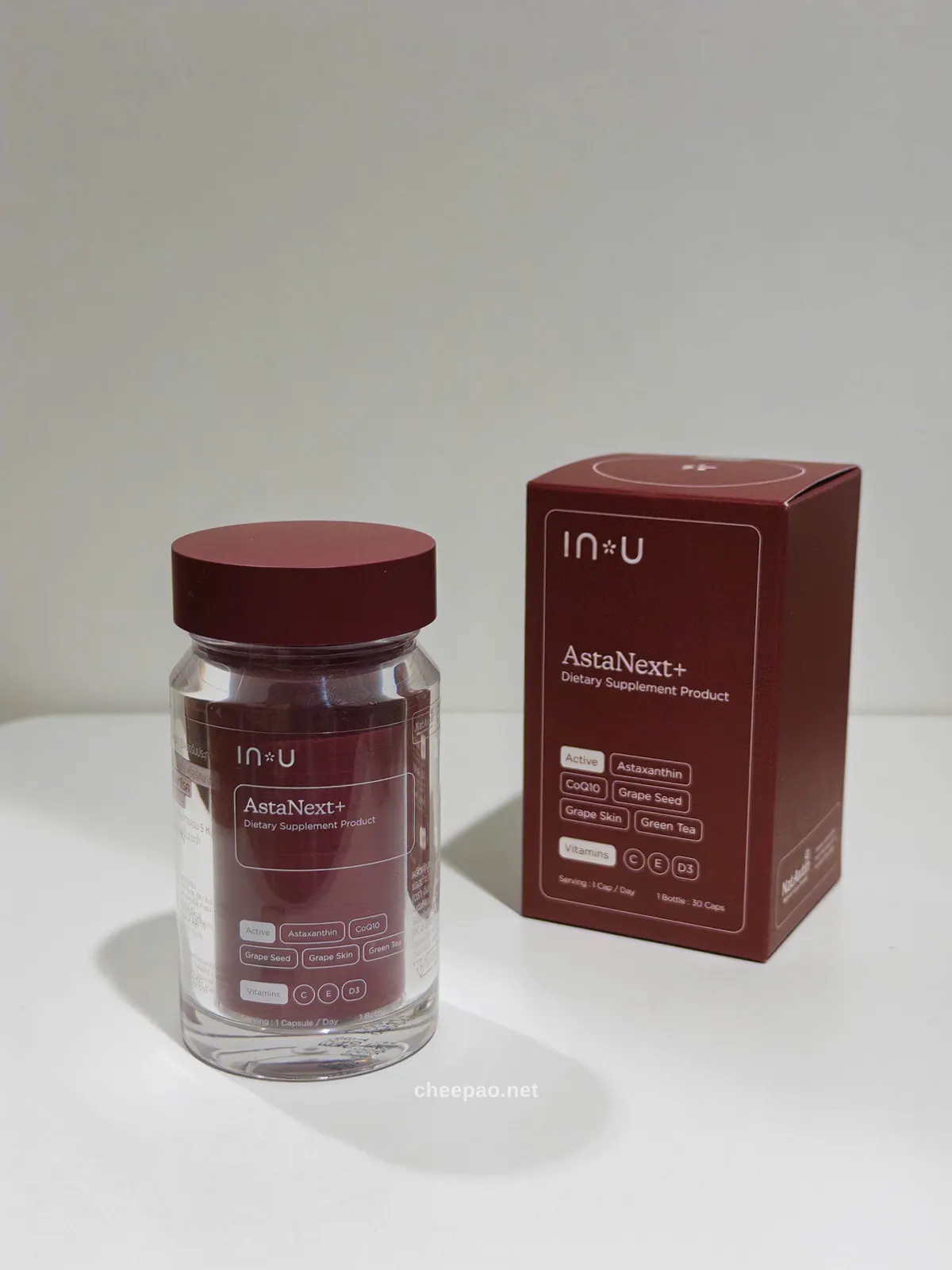 ขวดอาหารเสริม IN U AstaNext+ ขวดแก้วใสฝาสีไวน์ วางคู่กับกล่องที่ระบุ Active Ingredients: Astaxanthin, CoQ10, Grape Seed, Grape Skin, Green Tea และ Vitamins C, E, D3
